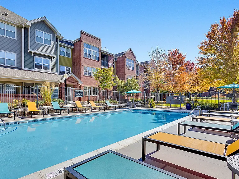 Inviting apartment view with a sparkling outdoor pool, vibrant lounge chairs, and colorful autumn foliage, promising a relaxing lifestyle.