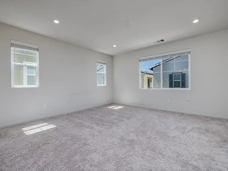 Another view of the spacious master bedroom showcasing multiple windows that fill the room with natural light. Soft carpet flooring and recessed lighting create a bright, comfortable atmosphere ideal for relaxation and modern living.
