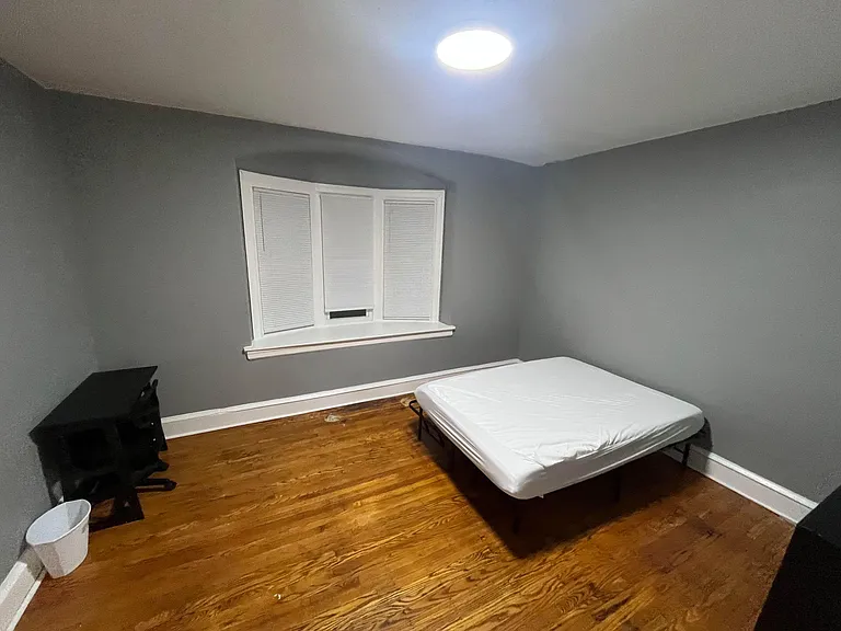 Private bedroom with hardwood floors, overhead lighting, and a window with blindsideal for a bed and small work setup.