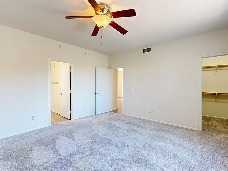 Spacious apartment bedroom with large closet, attached bathroom and plush carpet flooring.