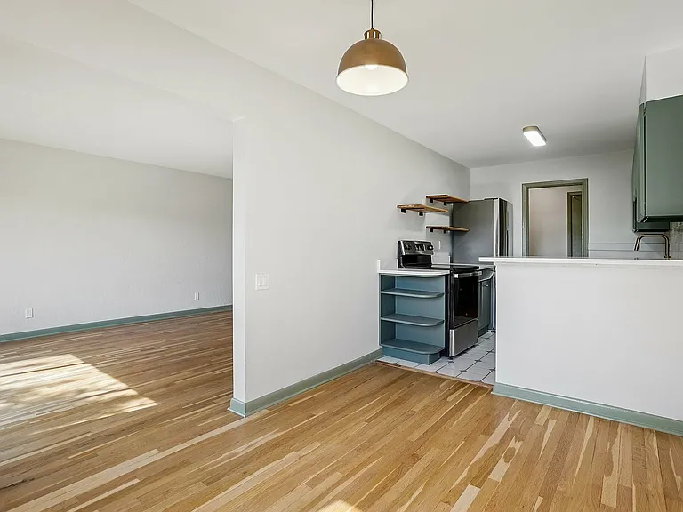 Modern apartment showcasing an open-concept kitchen with sleek appliances, natural wood flooring, and abundant light-filled living space.