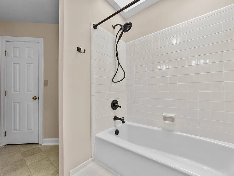Primary bath tub/shower with skylight, white tile surround, and dark bronze fixtures.
