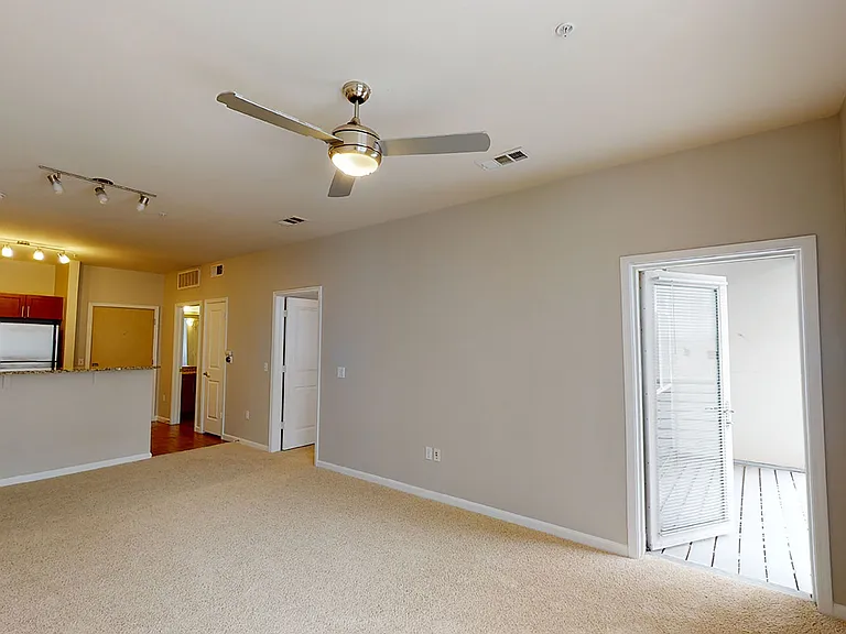 Apartment kitchen with stainless steel appliances, dining and living room with plush carpet flooring.