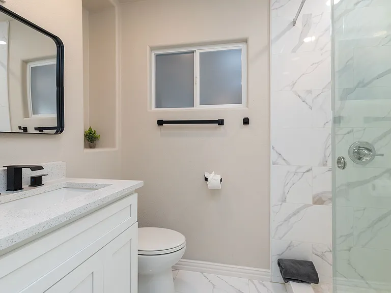 Relax in a modern, spa-style bathroom with a marble-tiled walk-in shower, sleek black fixtures, bright vanity lighting, and clean finishes. Directly connected to the primary bedroom for privacy and convenience.