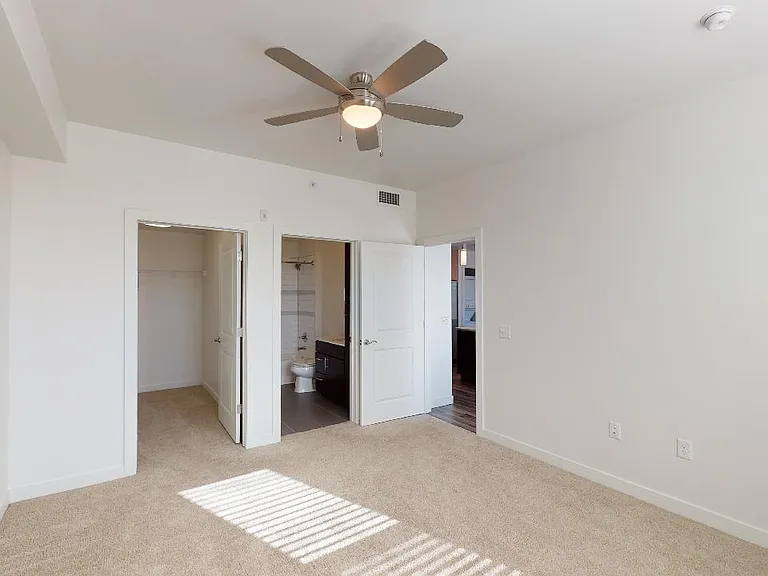 Spacious apartment bedroom with large closet, attached bathroom and plush carpet flooring.