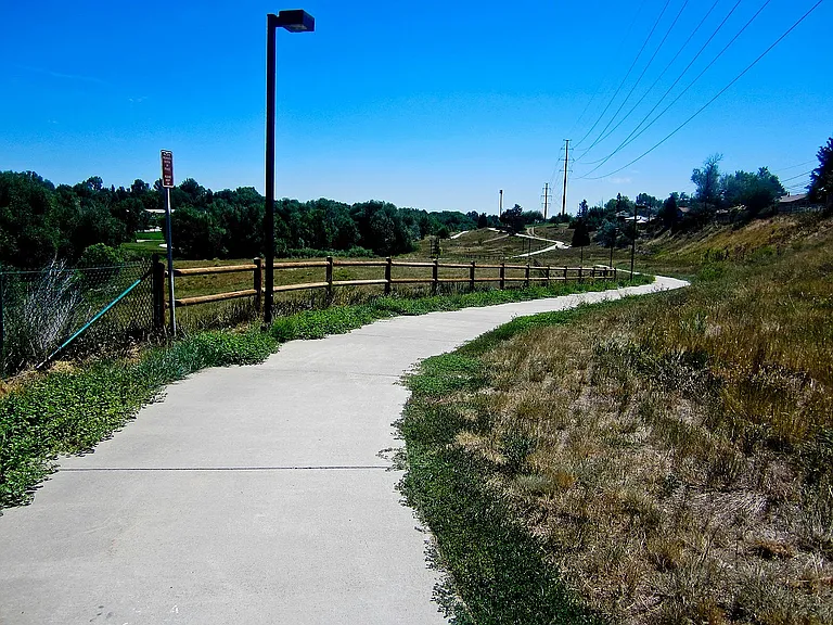 Scenic walking trail surrounded by lush greenery and a clear blue sky, perfect for outdoor enthusiasts.