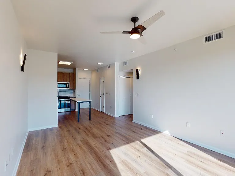 Apartment kitchen with stainless steel appliances, dining and living room with wood-style flooring.