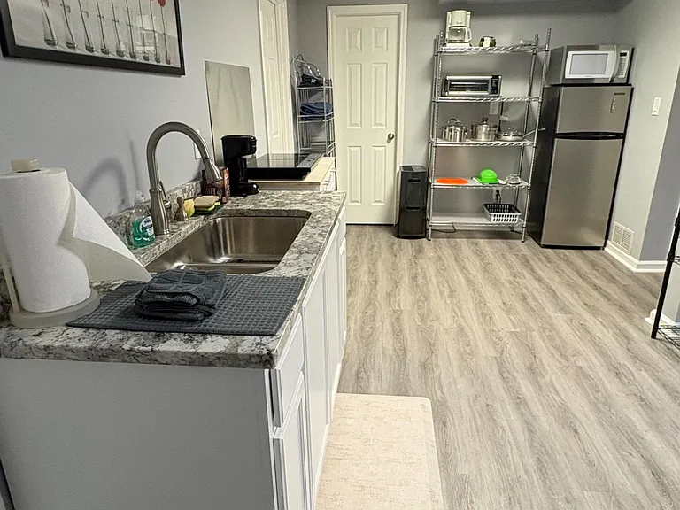 Efficient kitchenette with ample counter space, stainless sink, and a full-size fridge plus microwave and open shelving.