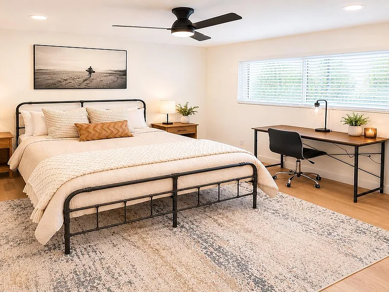 Spacious bedroom with a queen bed, dual nightstands, dedicated desk setup, and a mini fridge for added convenience.
