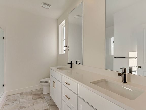 Modern bathroom with white cabinets, double sinks, black faucets, large mirrors, a glass shower encl
