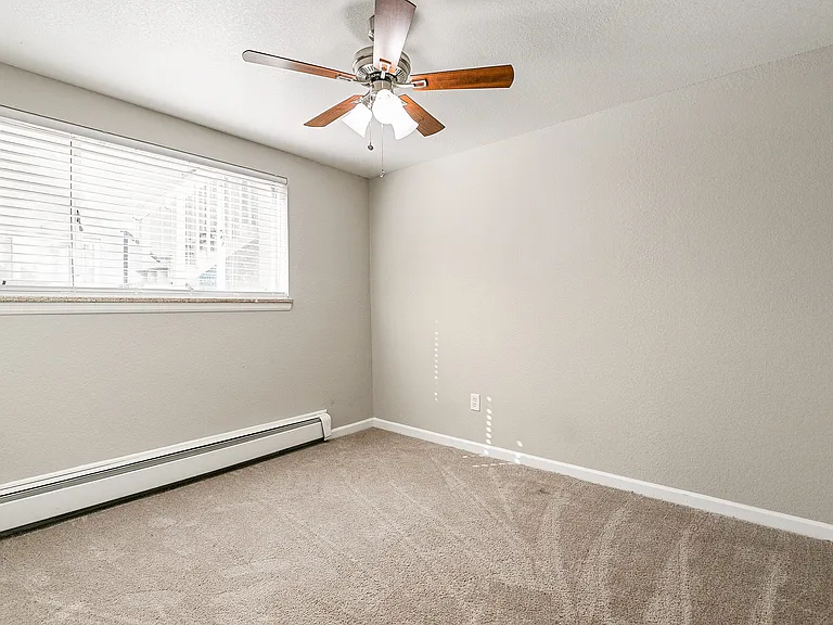 Bright and cozy bedroom with soft carpet flooring and a stylish ceiling fan, featuring a large window that invites natural light.