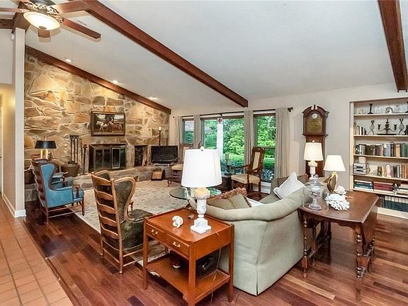 Living area featuring a stone fireplace, a ceiling fan, wood finished floors, and vaulted ceiling with beams