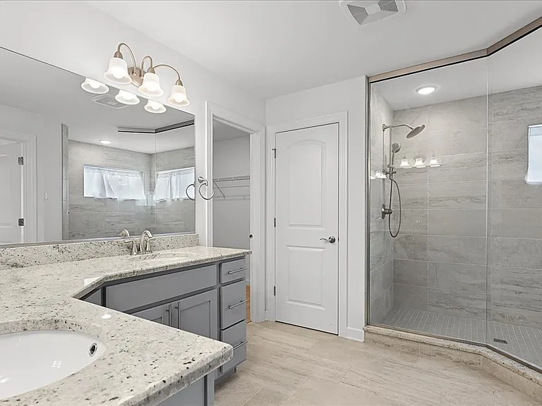 Primary bathroom with dual sinks, granite countertops, walk in shower, and walk in closet