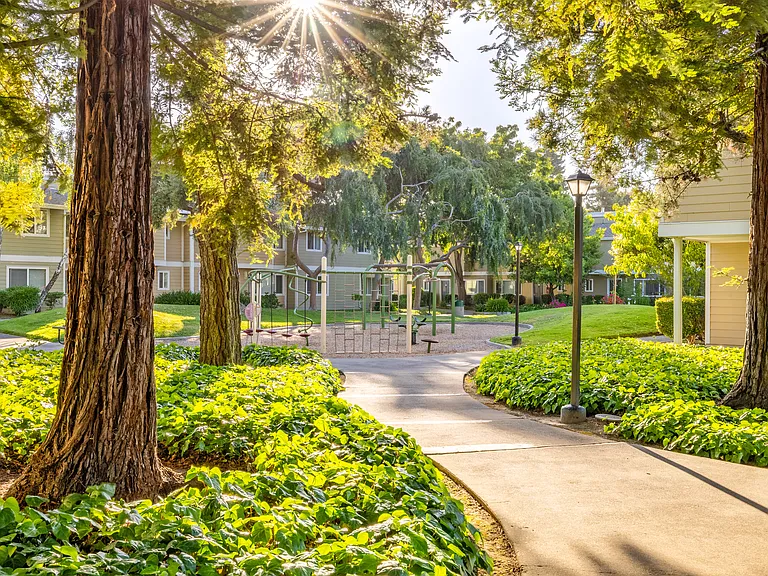 Shaded walking paths and mature trees lead to a charming playground in a lush, park-like setting.