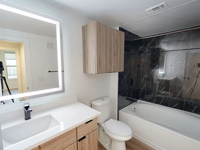 Apartment bathroom with large soaking tub, wood-style flooring and LED vanity mirror.