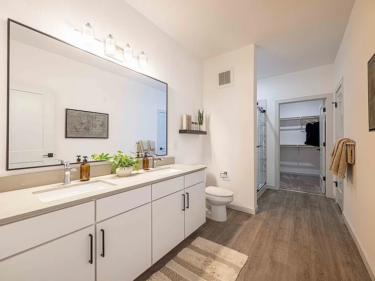The primary bathroom in this Garrett Parker B1 floor plan includes a double sink vanity, a private toilet area, and a walk-in closet just beyond.