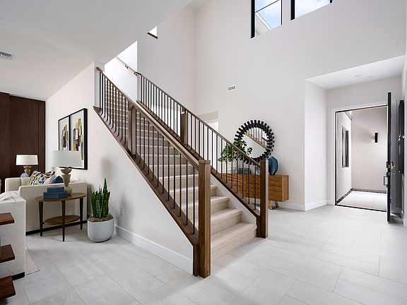 A spacious and modern entryway with a wooden staircase, decorative accents, and a view of an adjacen
