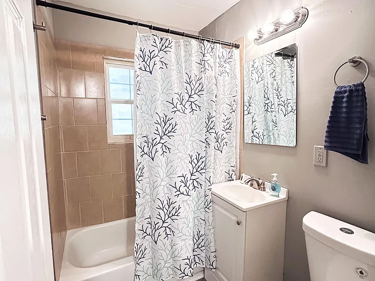 Full bathroom with a tub/shower combo, tiled surround, and vanity with mirror and overhead lighting for daily routines.