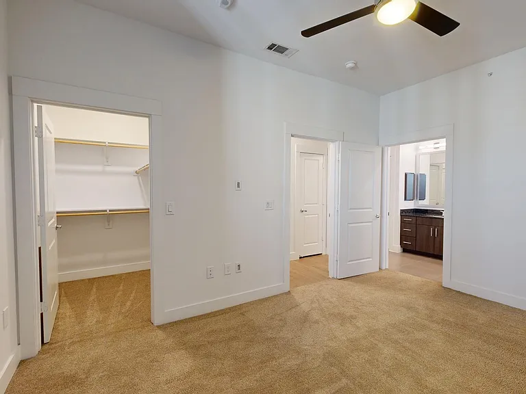 Spacious apartment bedroom with large closet, attached bathroom, and plush carpet flooring.