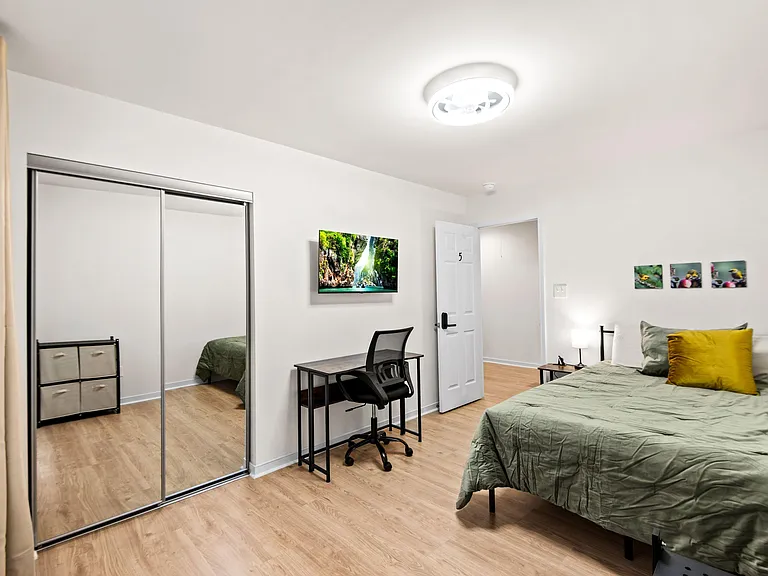 Private bedroom with mirrored closet doors, wood-look flooring, and a work desk plus nightstand lighting.