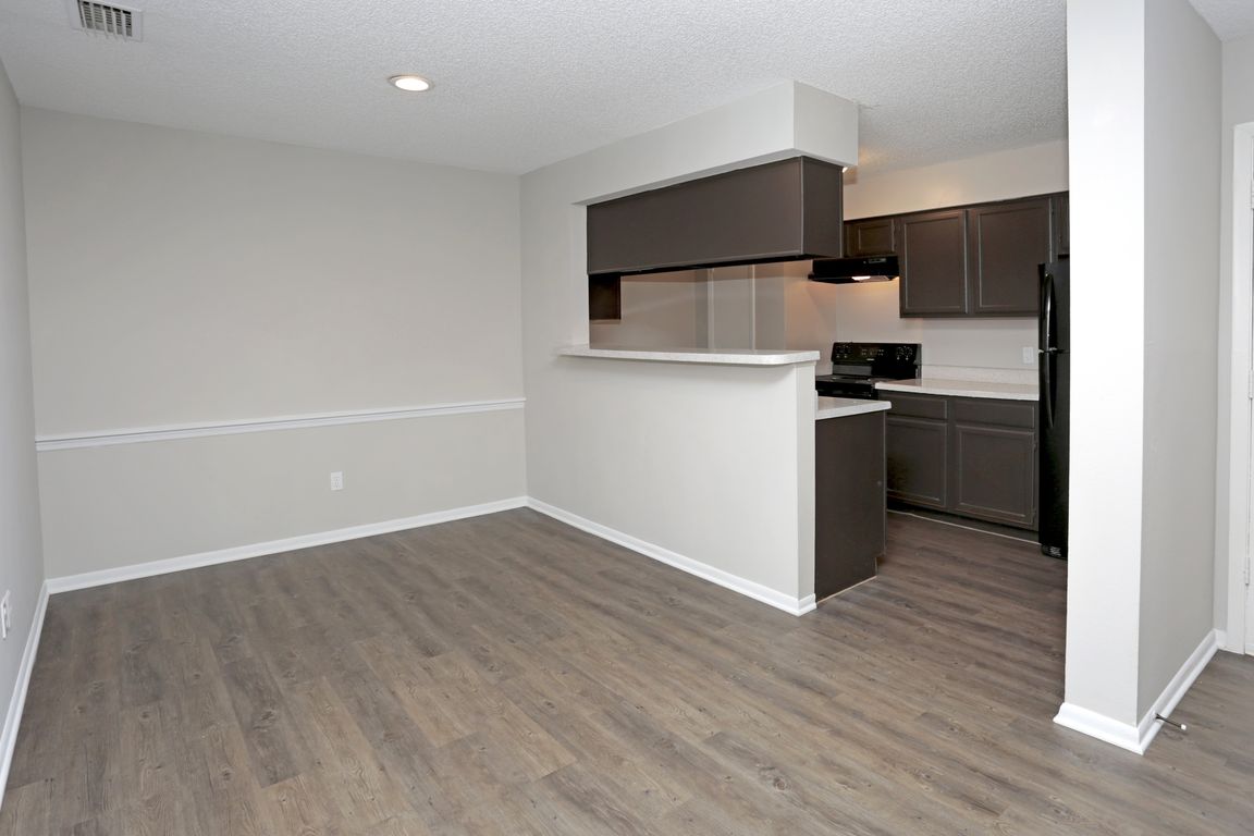 View of open dining area leading into a galley kitchen with bar-height counter and dark wood cabinets.