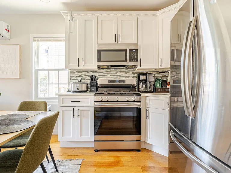 Updated kitchen with shaker cabinetry, stainless appliances, and mosaic tile backsplash, plus space for a dining table.