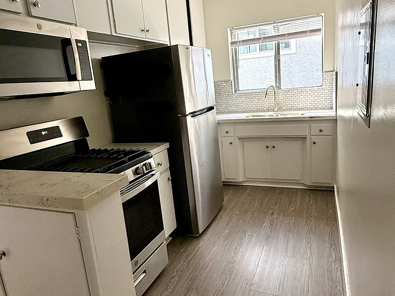 View of kitchen with stove, microwave, refrigerator, cabinetry, sink.