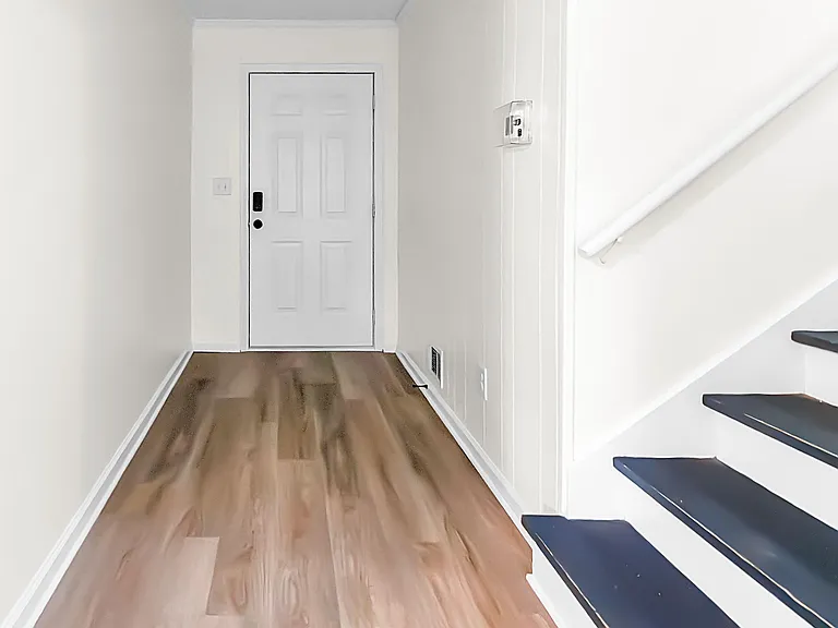 Clean entry hallway with durable wood-style flooring, secure front door access, and staircase leading to the next level.