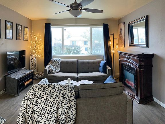 Living room facing east to street. A Samsung TV with remote, full sized electric fireplace, lighted tree, and designer lamp post shown with comfy throws, new vinyl and engineered flooring plank, etc.