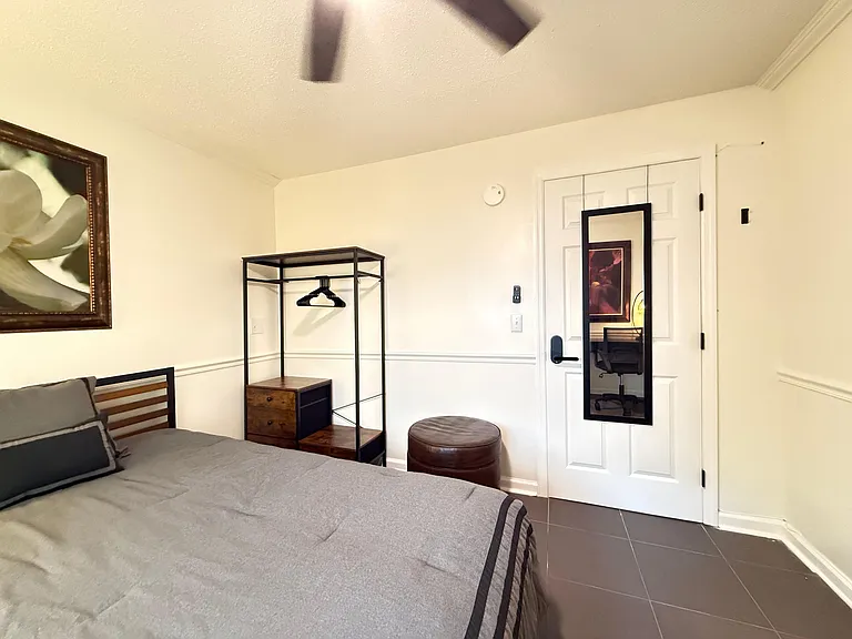 Furnished bedroom with a comfortable bed, ceiling fan, and convenient open closet rack with drawer storage and mirror.