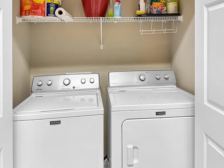 Dedicated laundry closet with side-by-side washer and dryer plus a wire shelf for detergent and household storage.