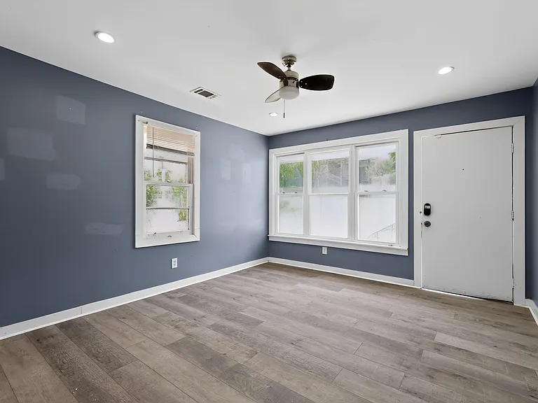 Versatile room with durable wood-look flooring, ceiling fan, and large windows that bring in natural light.