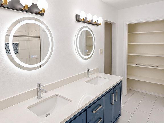 Updated bathroom features a dual-sink vanity with quartz-style counters, illuminated mirrors, and a large walk-in linen close