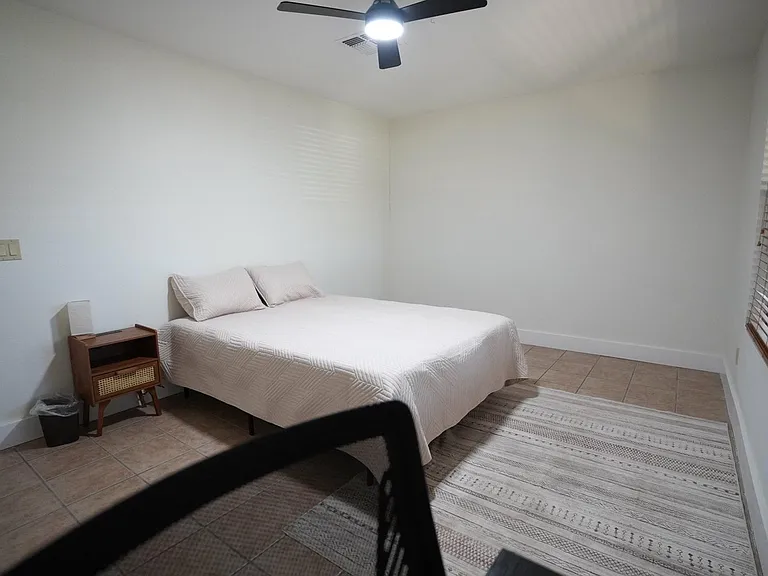 Spacious bedroom with a queen bed, ceiling fan, tiled floors, and a large window with blinds for easy light control.