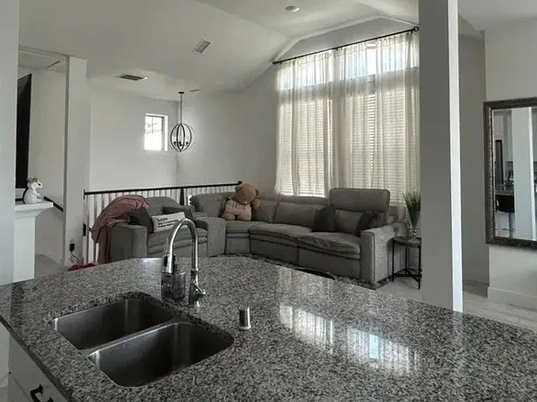 Open-concept living area with a large sectional, high ceilings, and tall windows, flowing into a spacious kitchen island.