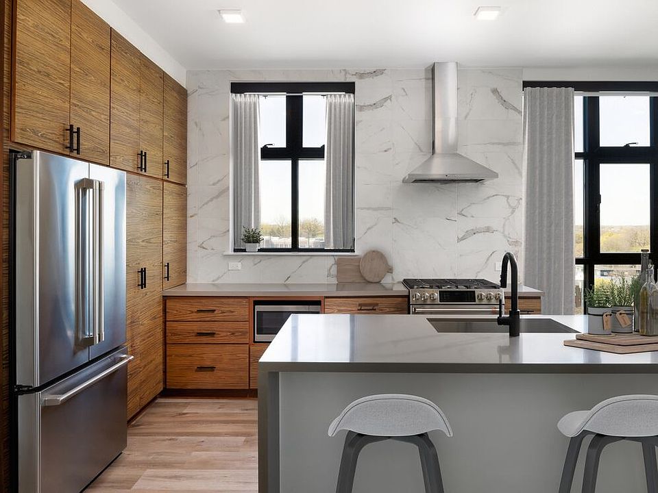 Kitchen with wood cabinetry, grey quartz countertops, marble backsplash, stainless steel appliances, and hard surface flooring