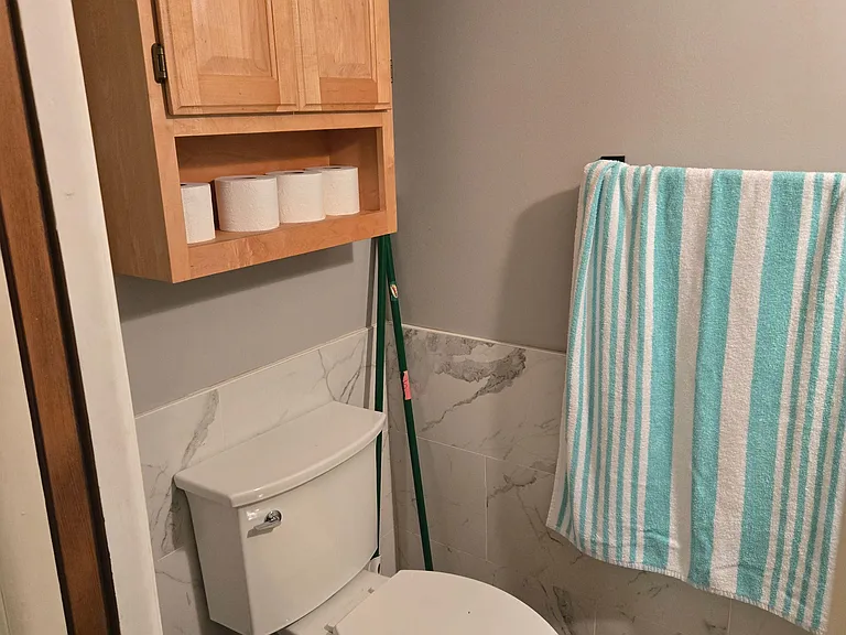 Bathroom with tiled surround, towel bar, and wall-mounted storage cabinet for toiletries and linens.