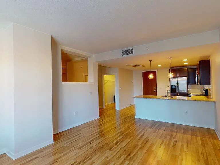 Apartment kitchen with stainless steel appliances, dining and living room with wood-style flooring.