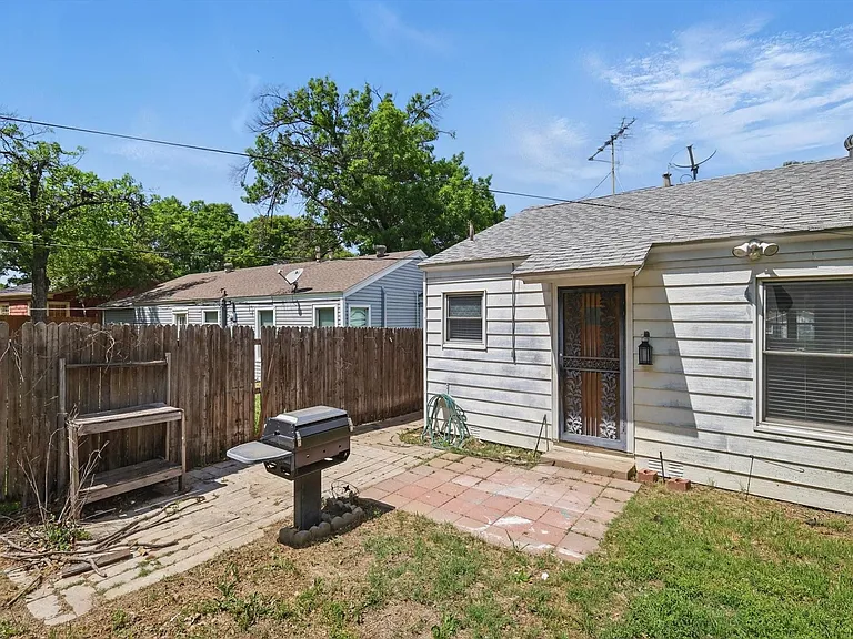 Expansive backyard with a paver patio, established trees providing natural shade, and a storage shed. Grill is non-functioning.