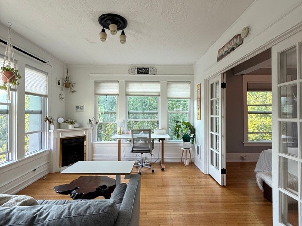 NW facing living room with 6 big windows with hillside views, a gas fireplace, an adjustable desk, a pull-out sofa, a wood slab coffee table, an adjustable side table, with french doors to the bedroom