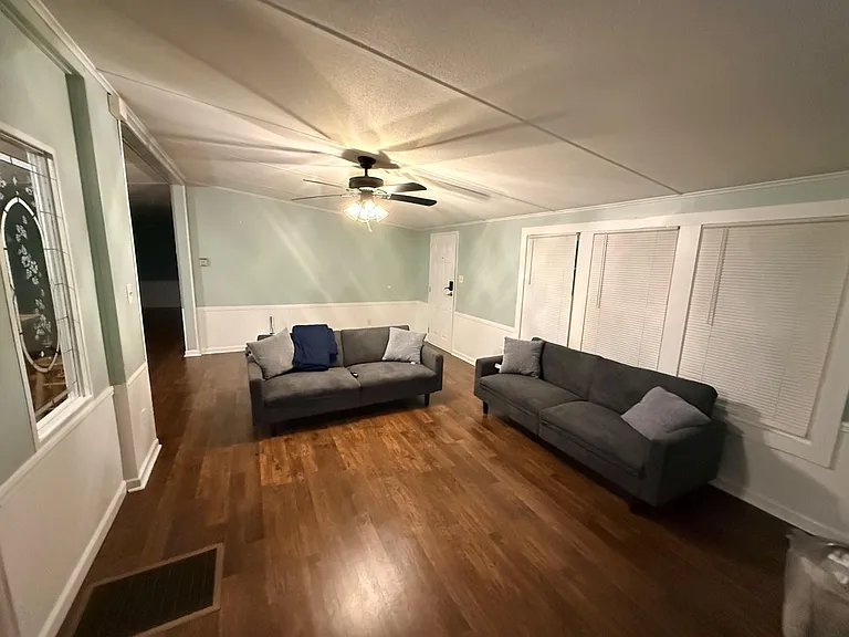 Spacious living room with hardwood floors, ceiling fan lighting, and multiple windows with blinds for added privacy.