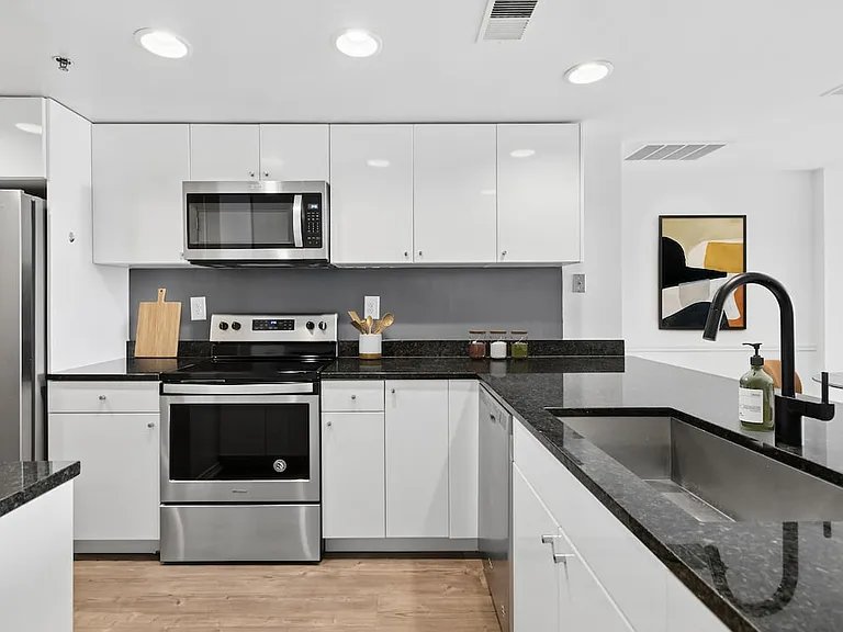 Renovated Package I kitchen with white cabinetry, black granite countertops, stainless steel appliances, and hard surface flooring