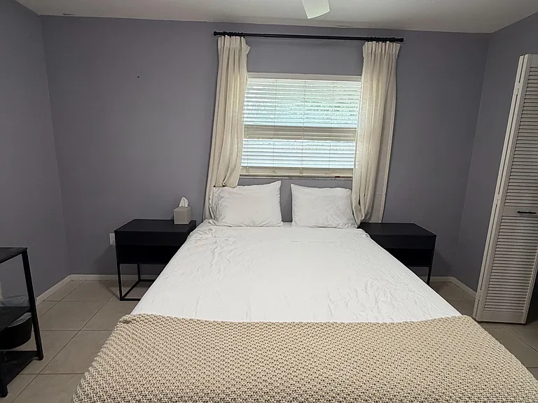 Private bedroom featuring a ceiling fan with light, window with blinds and curtains, and space for a full/queen bed.