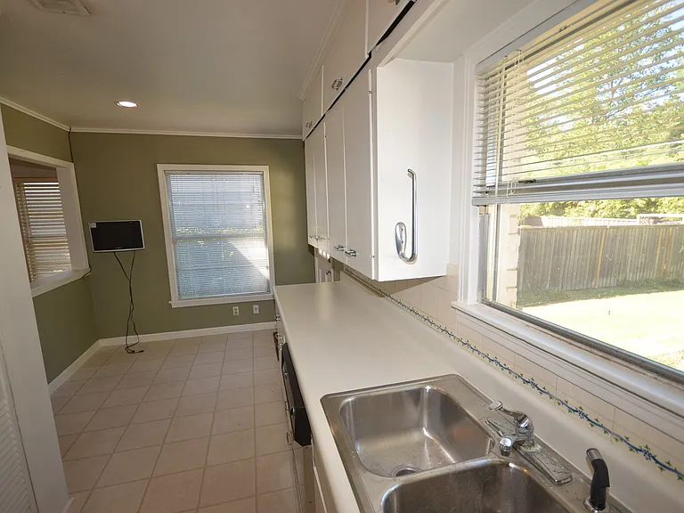 Kitchen space featuring a double basin stainless steel sink, white cabinetry, and light-toned tile flooring.