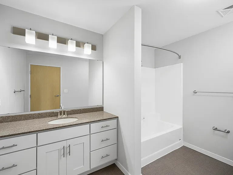 Sleek contemporary bathroom featuring a spacious vanity with a granite countertop, modern lighting, and a clean white bathtub. Sleek contemporary bathroom featuring a spacious vanity with a granite countertop, modern lighting, and a clean white bathtub.
