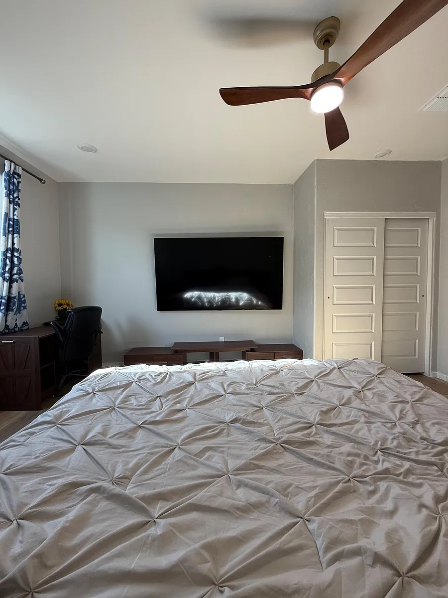 Spacious bedroom featuring a ceiling fan, wall-mounted TV, desk nook, and sliding closet doors for easy storage. - W Thurman Dr