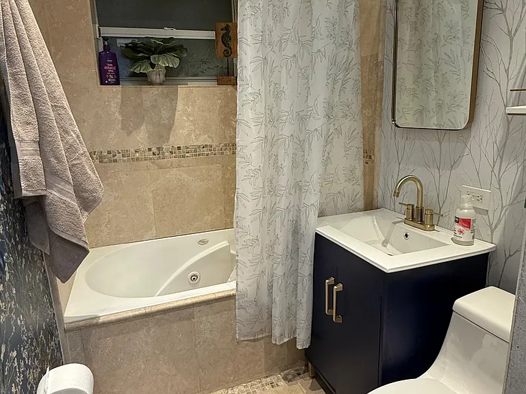 Full bathroom with tiled tub/shower combo, vanity sink with storage, and a wall mirror for daily routines.