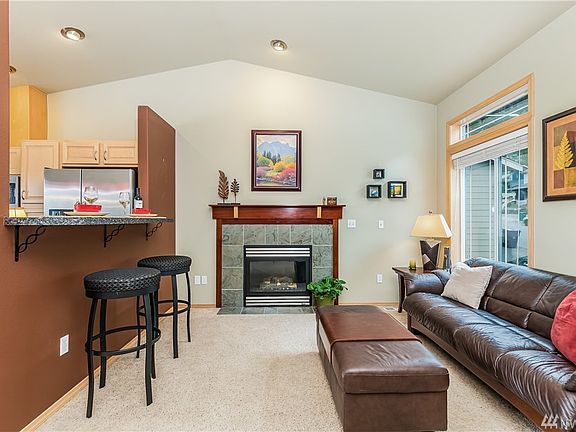 Living Room features Fireplace w/Gas Log, Ceramic Tile Surround & Hearth with Elegant Handcrafted Wood Mantle.  Wood Wrapped Windows w/White Blinds & Bar Dining Space - Perfect for Entertaining.