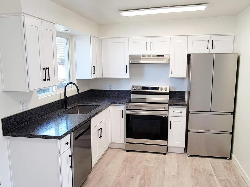 Window over the sink in the kitchen with charcoal, honed granite, bright white cabinets, and brand new stainless steel appliances
