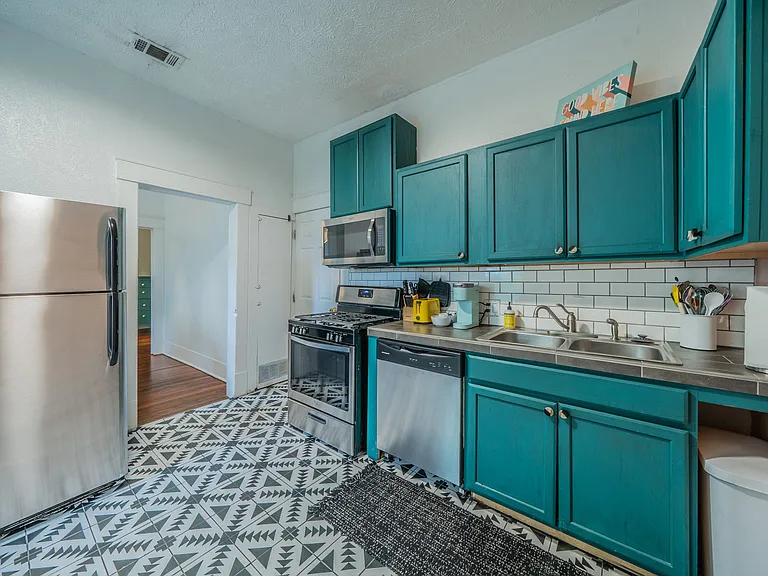 Modern full kitchen with teal cabinets and stainless steel appliances.